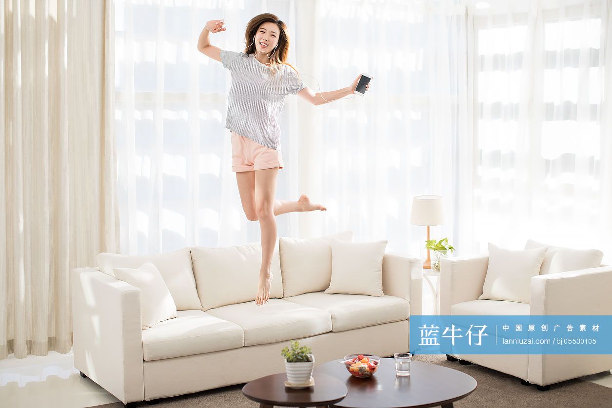 年轻女子在沙发上听音乐蹦跳