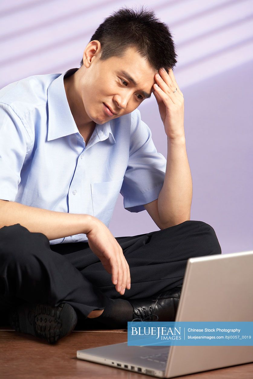 Chinese Man Sitting On Floor With A Computer Looking Frustrated