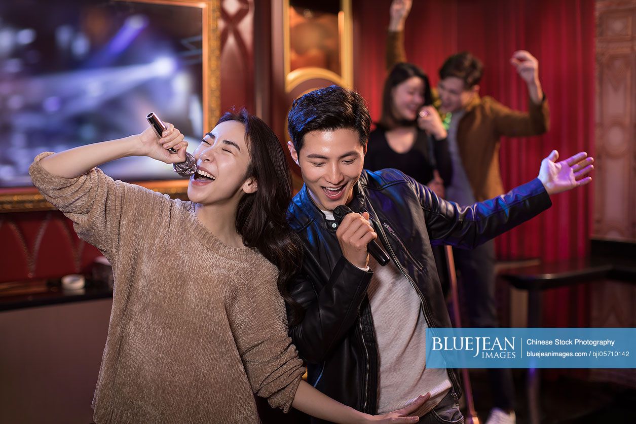 Happy Chinese young couple singing karaoke in nightclub