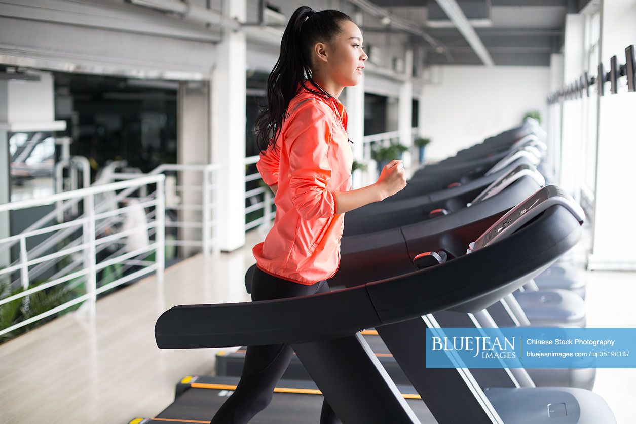 Young Chinese woman running on treadmill in gym