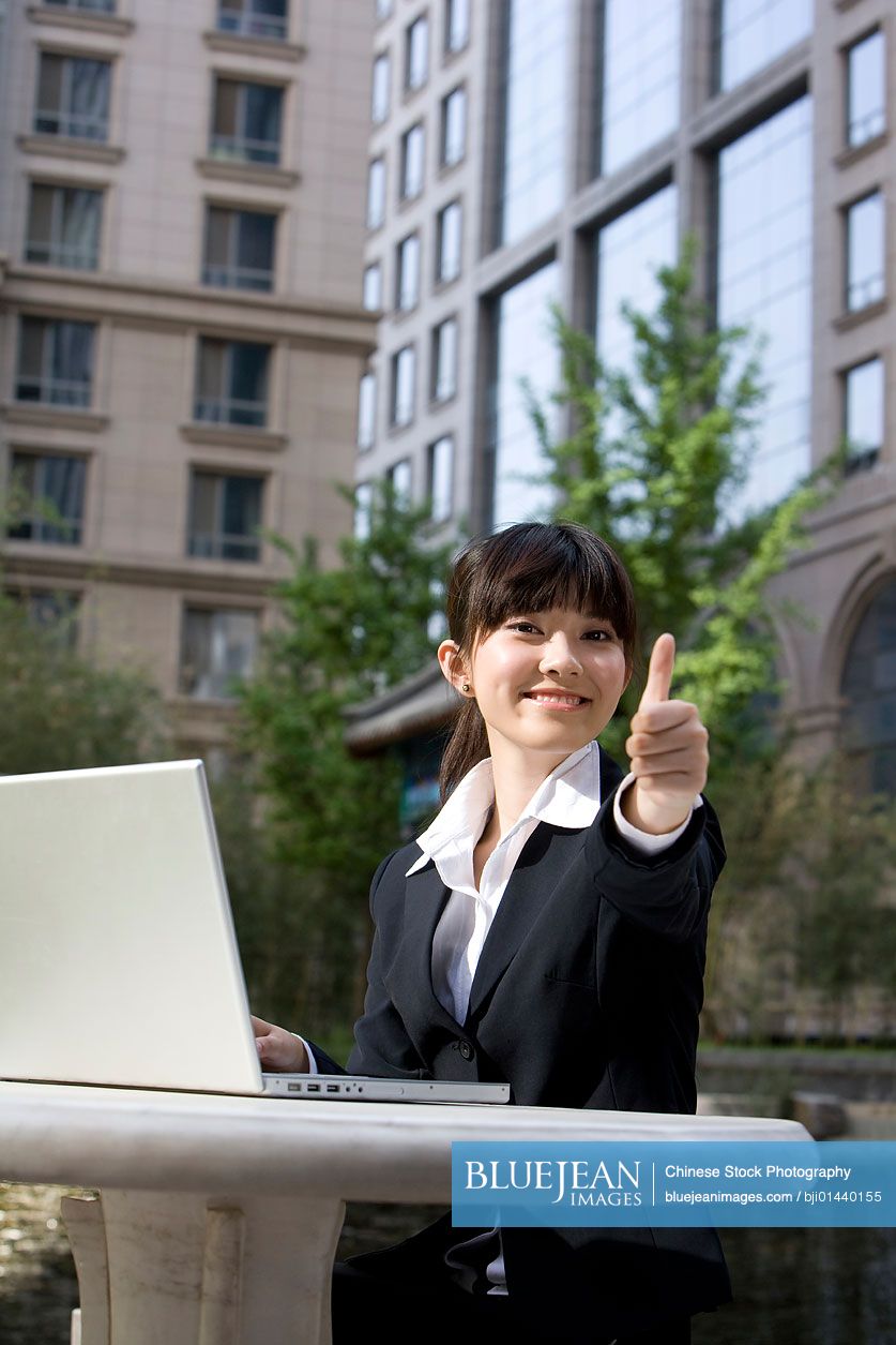 Chinese businesswoman giving thumbs up in front of computer