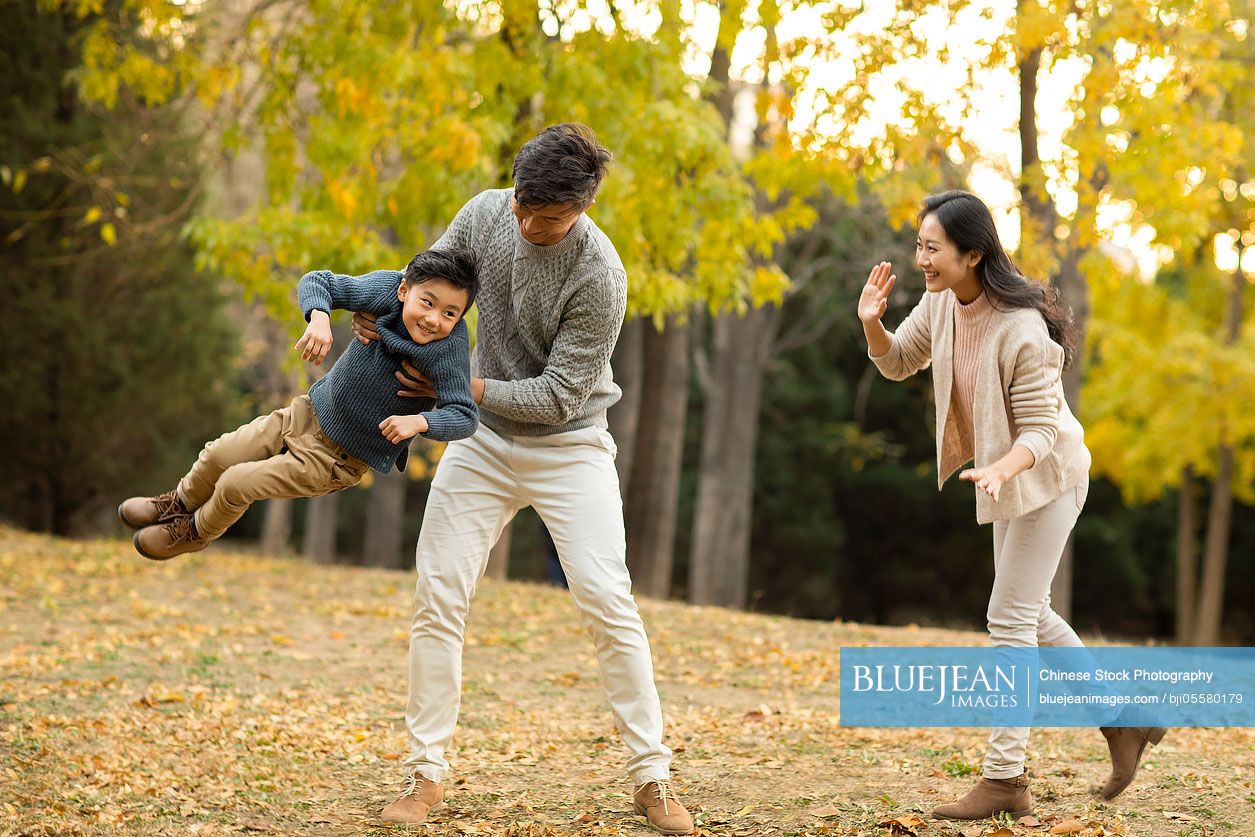 Happy young Chinese family playing in autumn woods