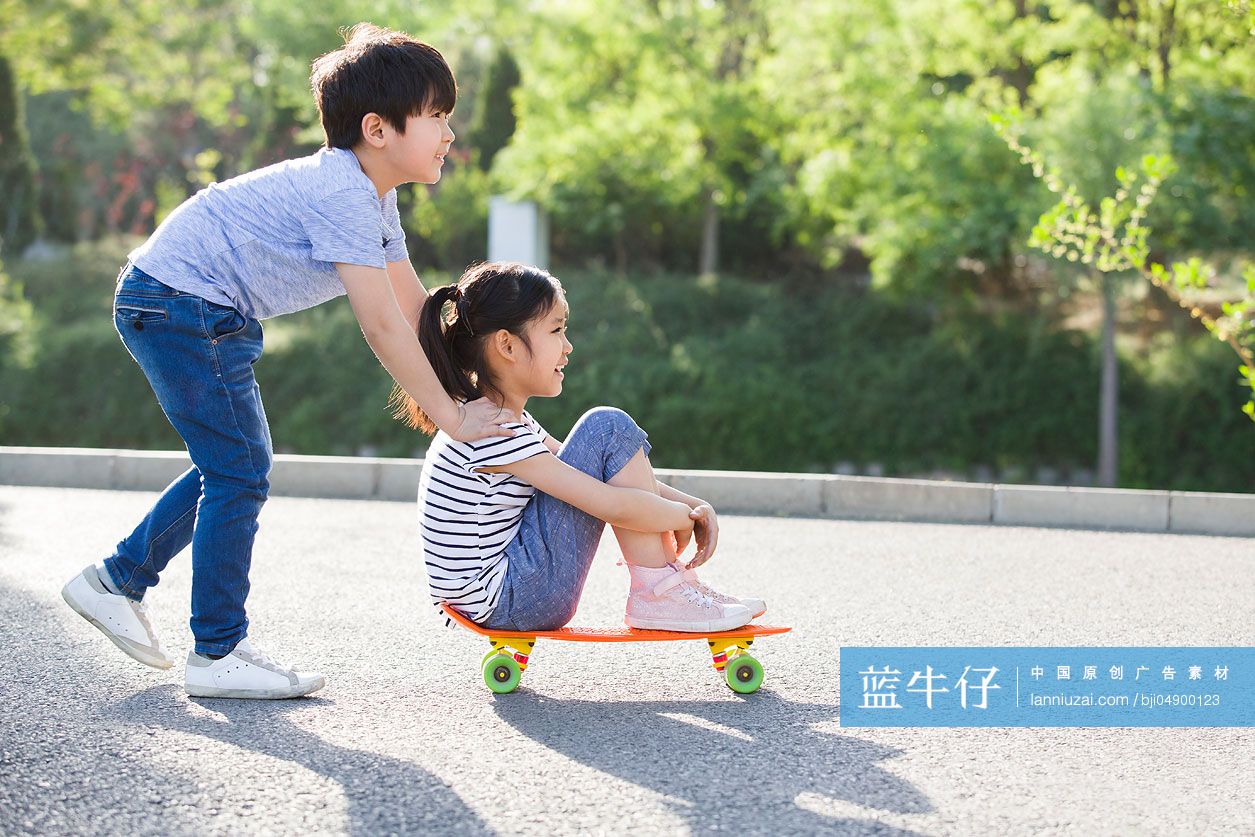 男孩推着坐在滑板上的女孩向前走