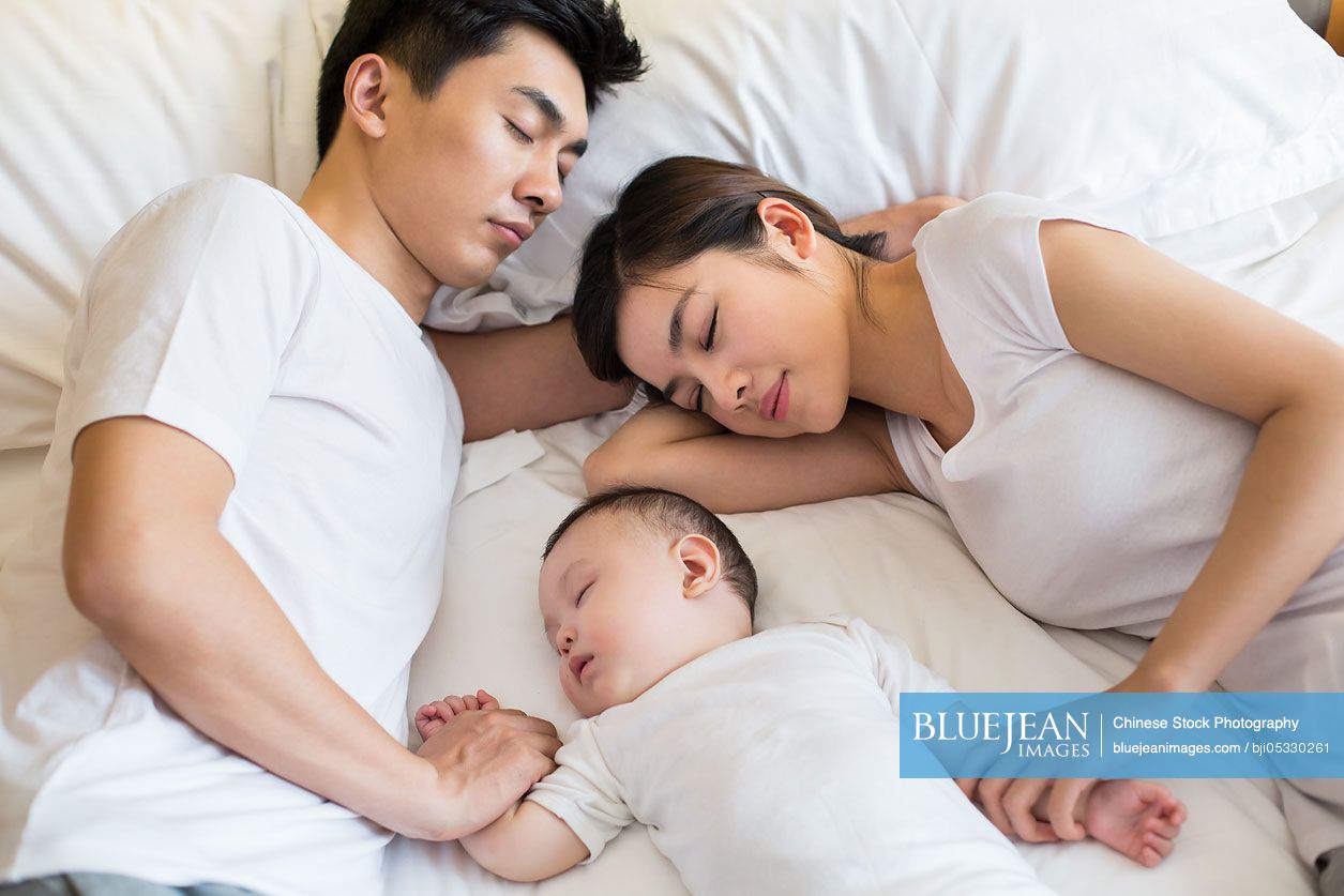 Young Chinese family sleeping in bed