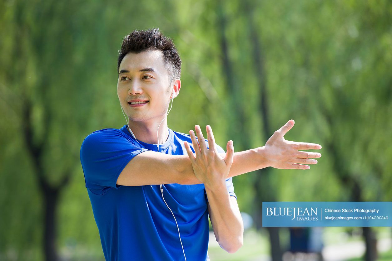 Young Chinese man stretching and listening to music in park