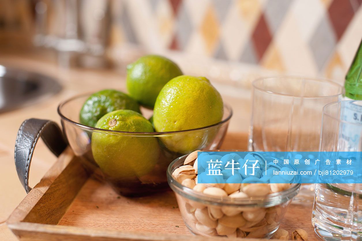 Close-up of oranges and pistachios in bowls against blurred backsplash on kitchen counter