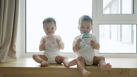 Two twin babies drinking water from their bottles