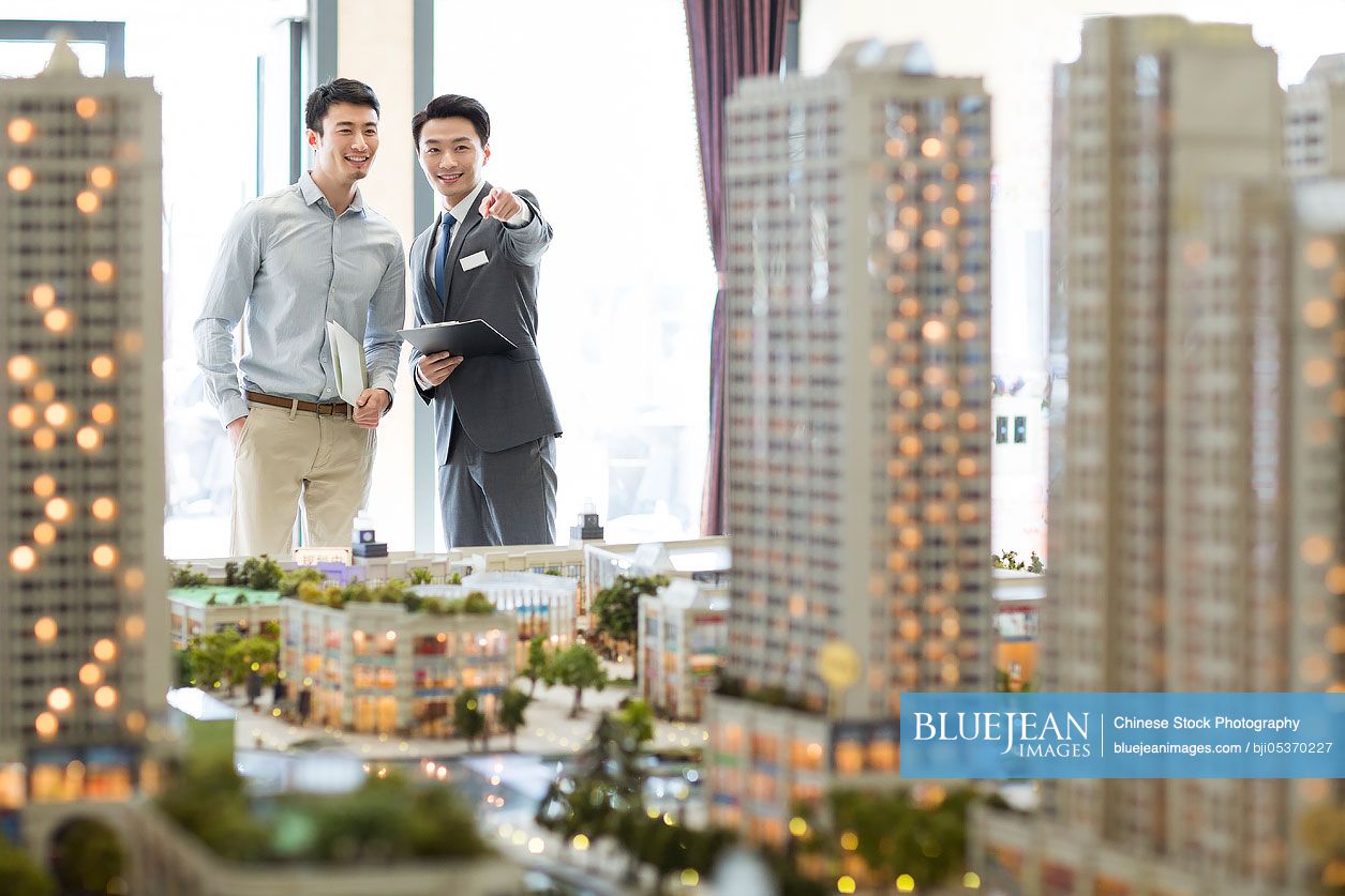 Chinese realtor showing architectural model to young man