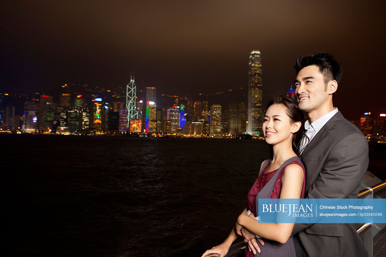 Happy young Chinese couple enjoying the night view of Victoria Harbor, Hong Kong