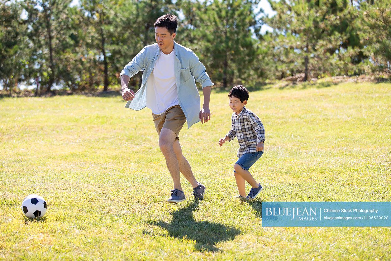 happy-chinese-father-and-son-playing-football-in-park-high-res-stock