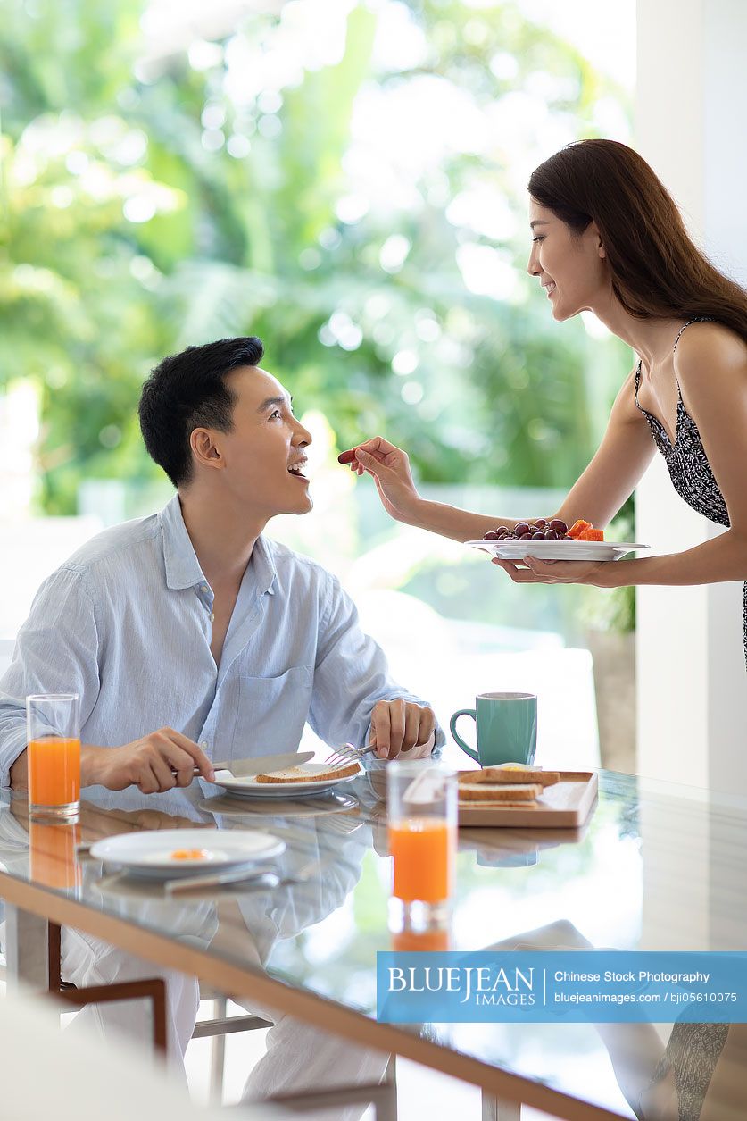 Happy young Chinese couple having breakfast in hotel room