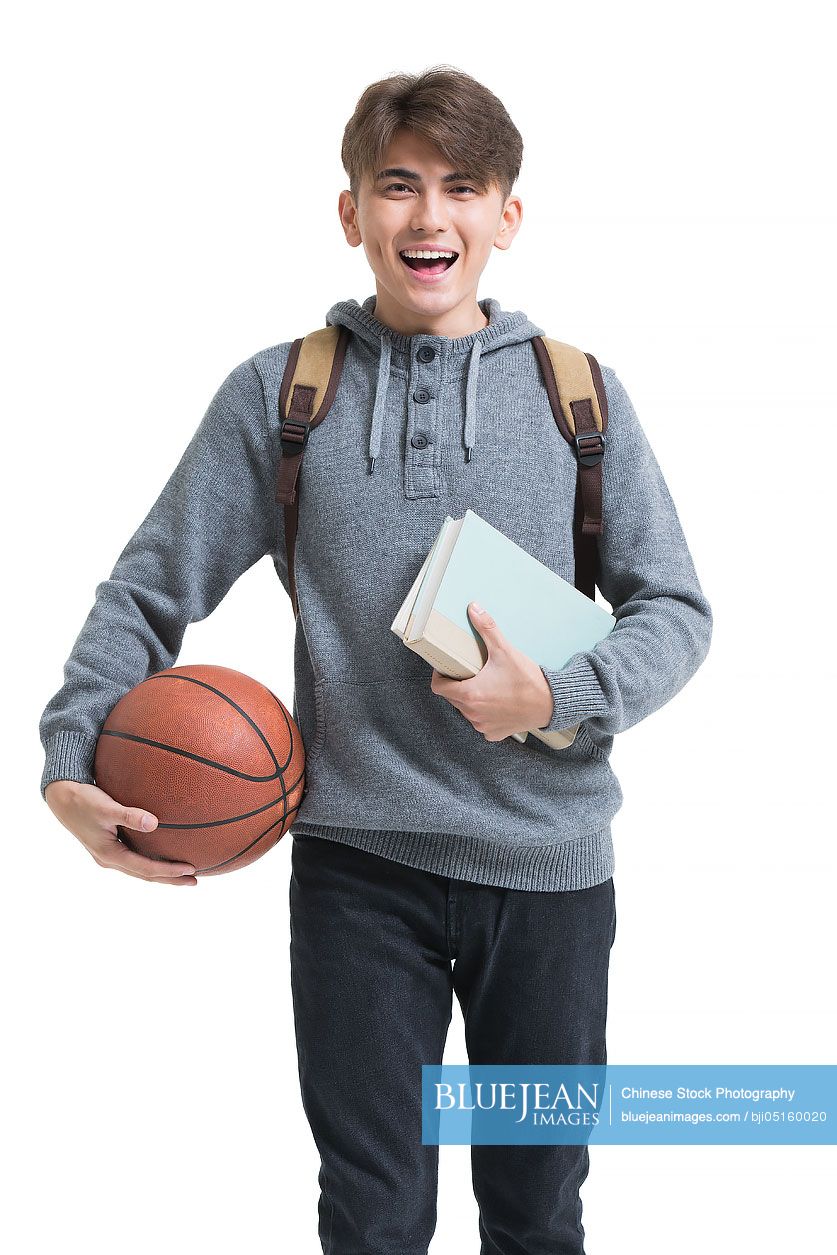 Cheerful male college student holding books and basketball