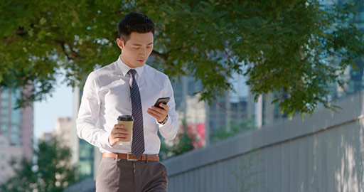 Young Chinese businessman walking with coffee and cellphone on street,4K