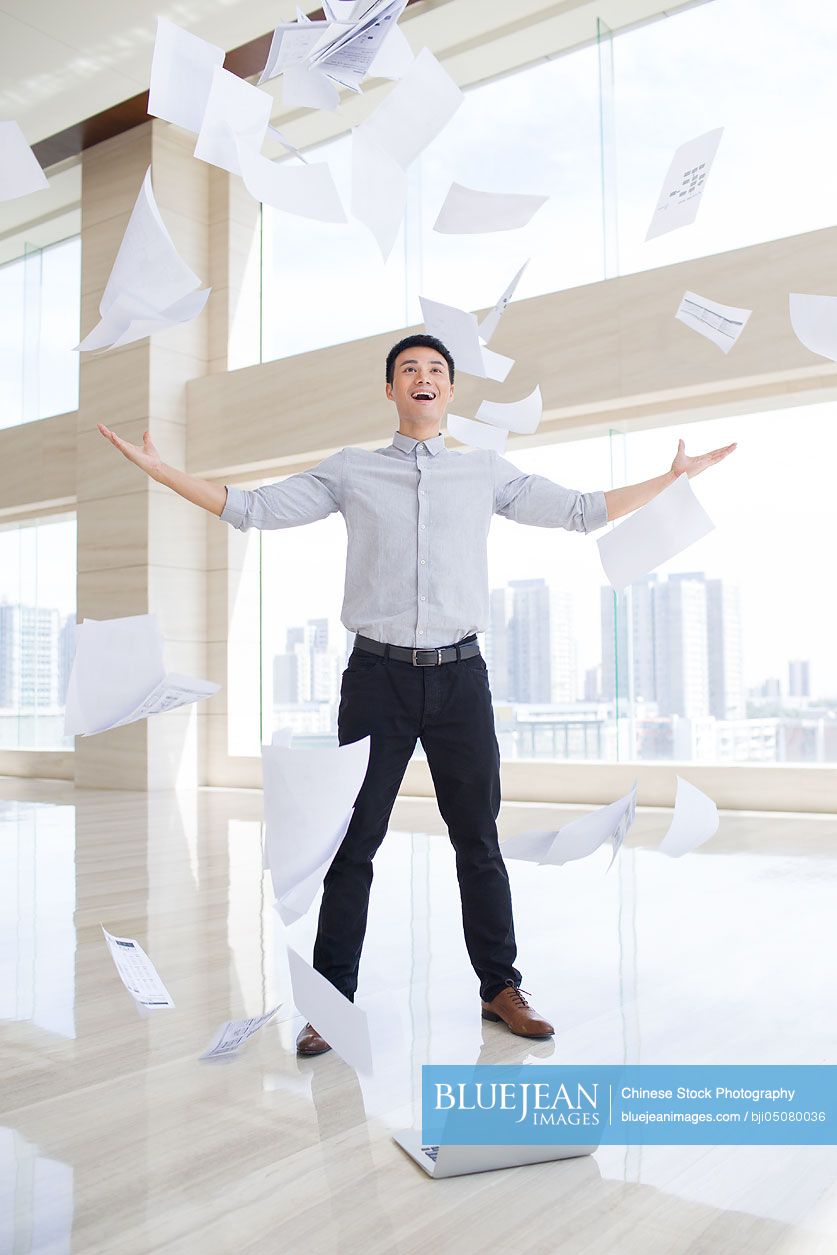 Young Chinese businessman throwing paper in the air