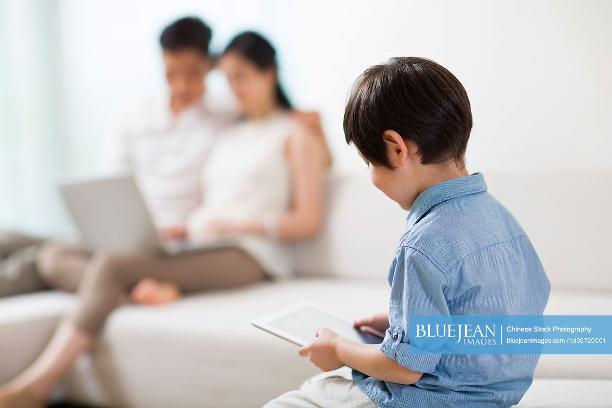Happy young Chinese family using digital gadgets at home