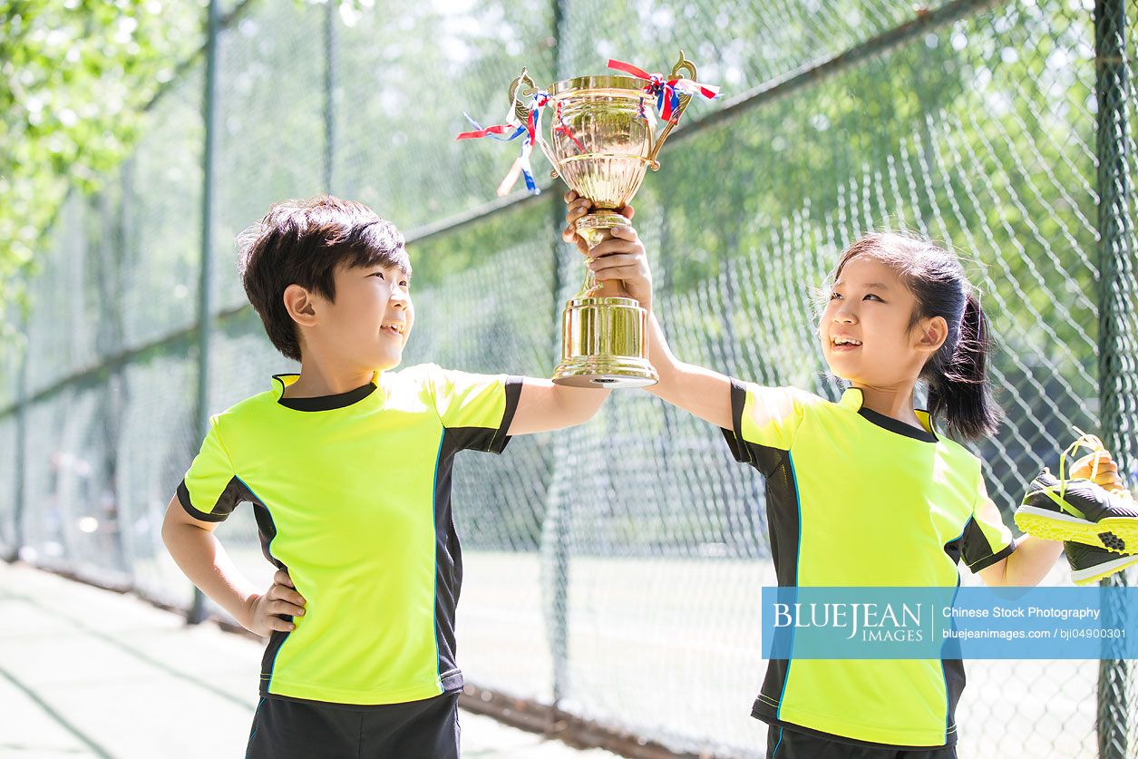 Happy Chinese children in sportswear showing their trophy