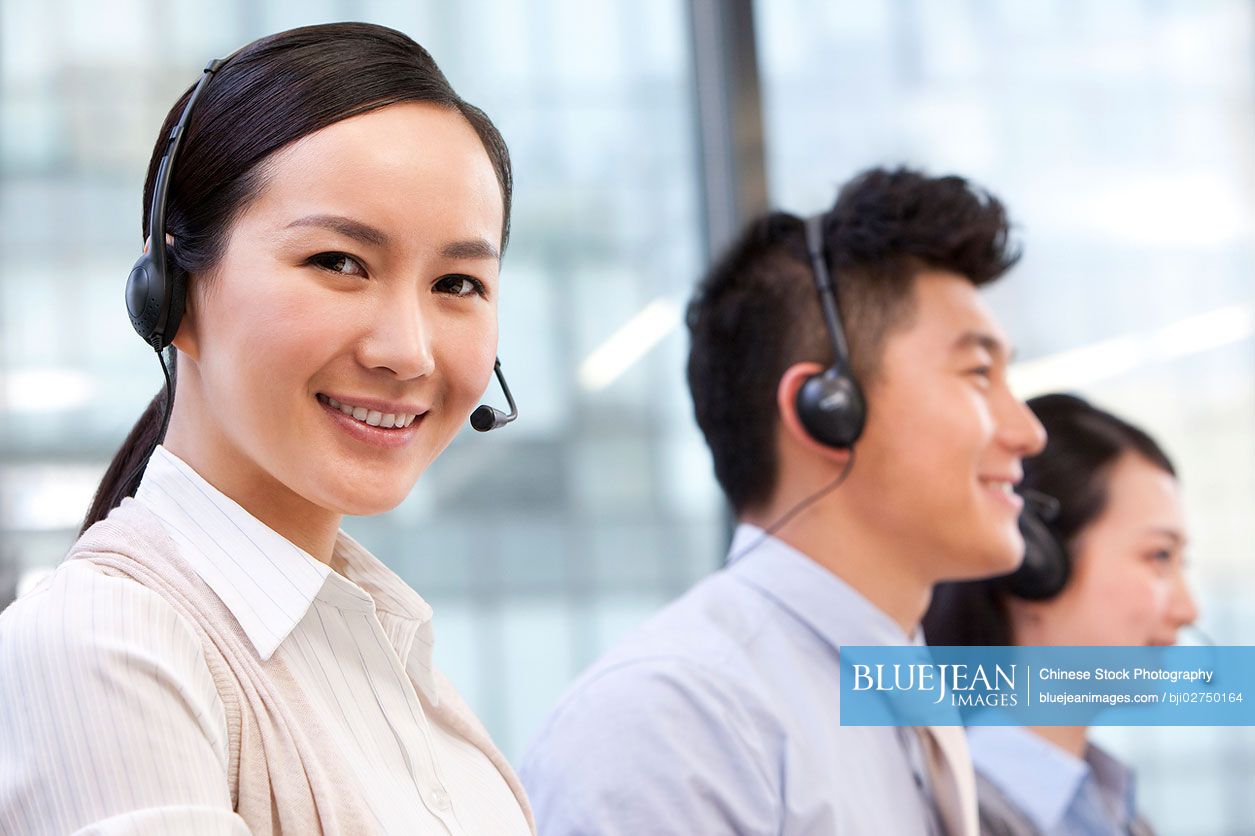 Smiling Chinese call center agent with her colleagues in the background