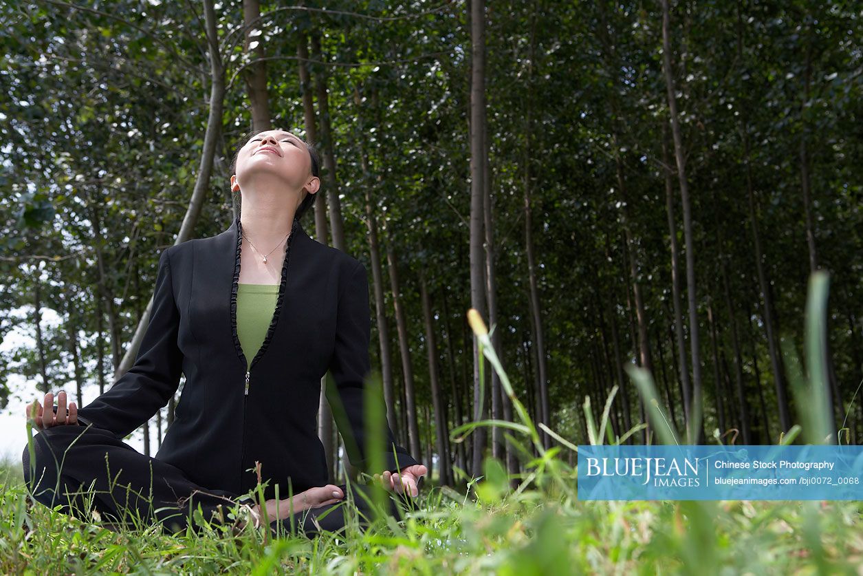 Chinese businesswoman sitting down in field, meditating