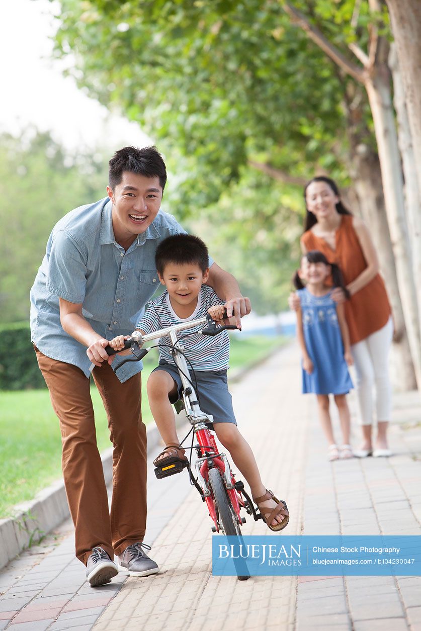 Young Chinese father teaching his son to ride a bicycle