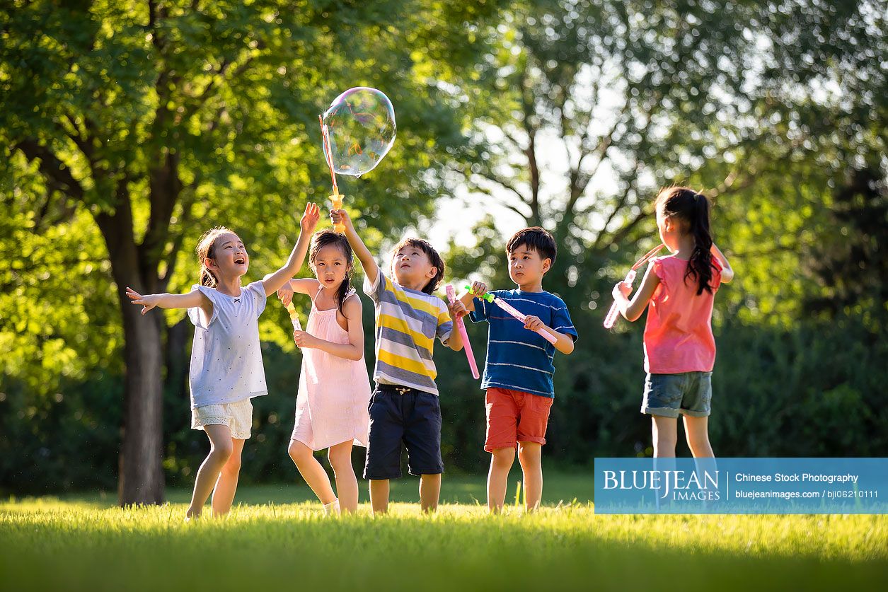 Happy Chinese children blowing bubbles on meadow