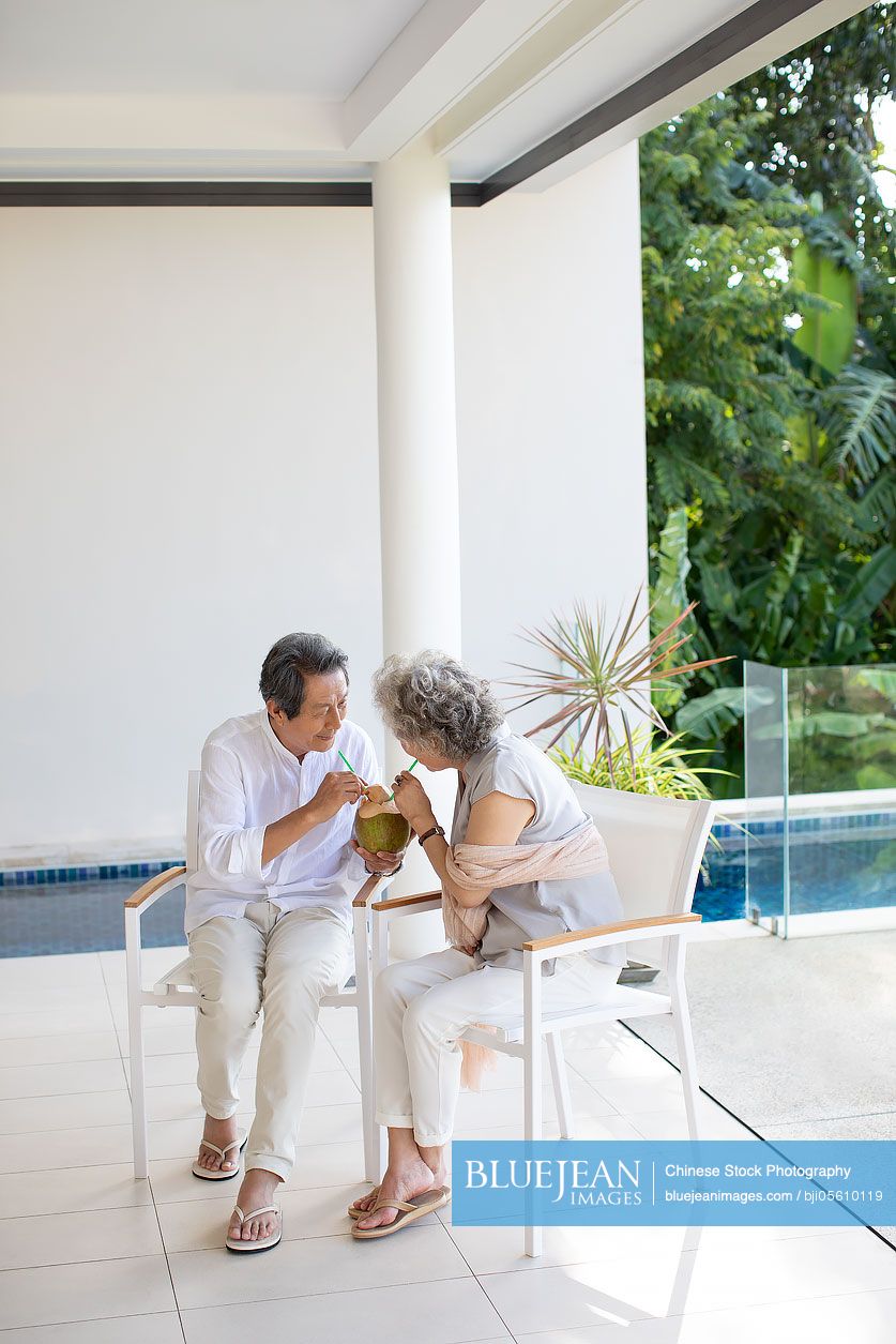 Happy senior Chinese couple drinking coconut milk on balcony