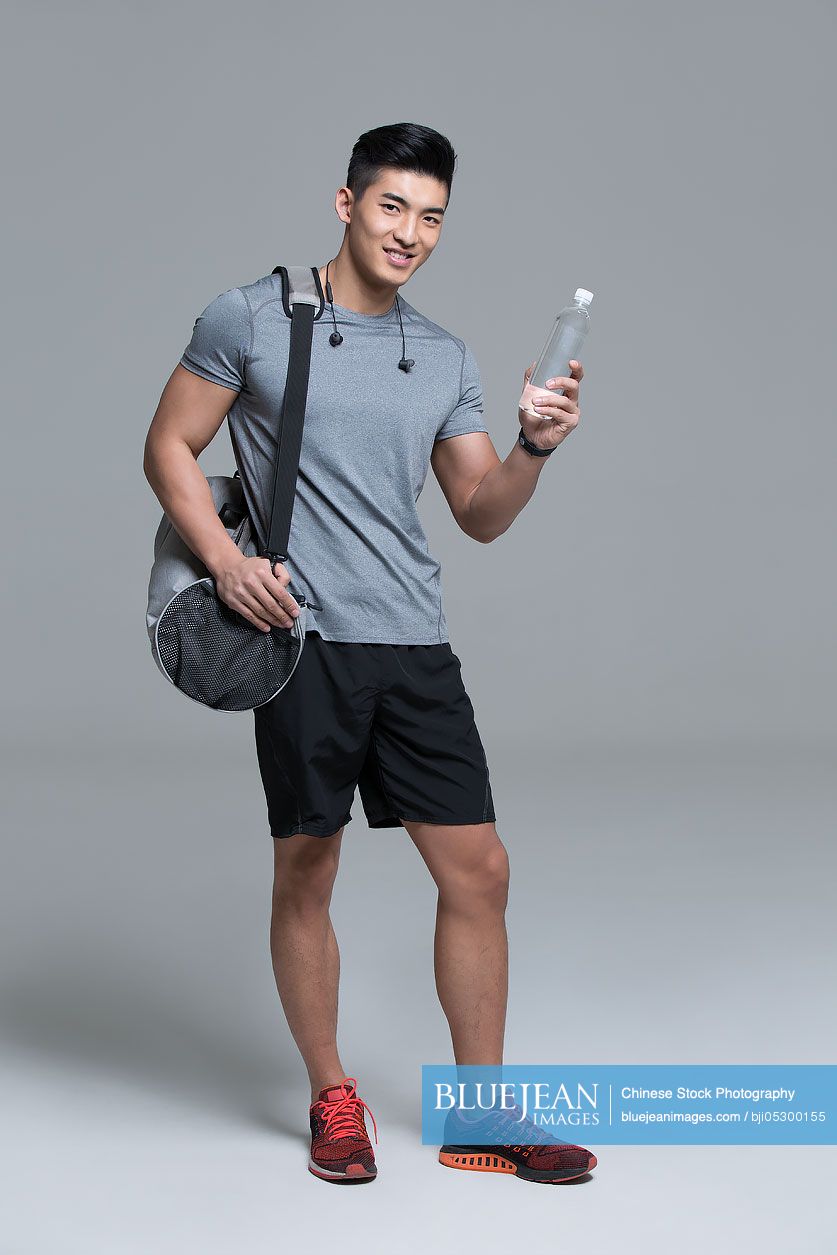 Cheerful young Chinese male athlete holding a bottle of water