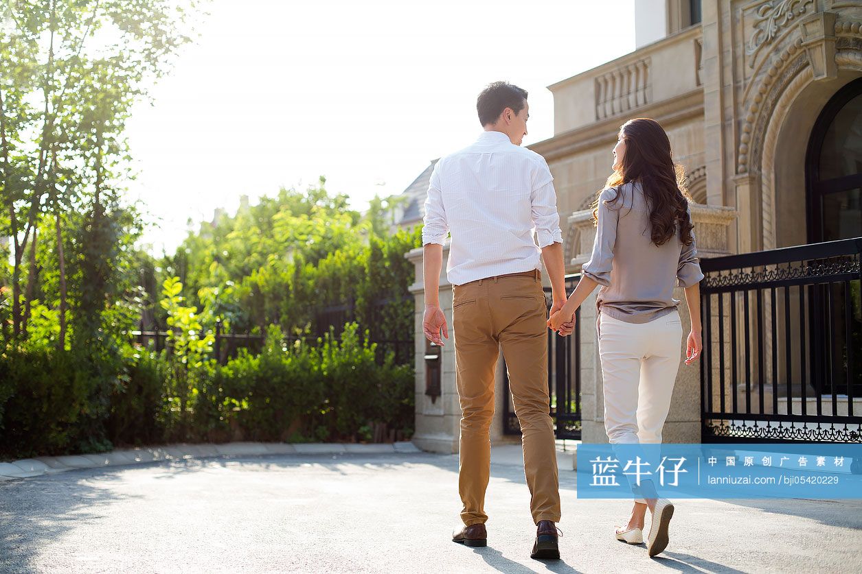 快乐的年轻夫妇手牵手在别墅外散步