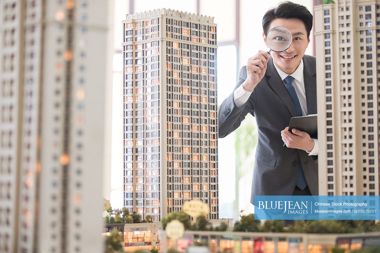 Chinese realtor checking architectural model through magnifying glass