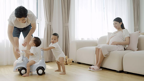 Parents watching their twin babies play with a baby vehicle