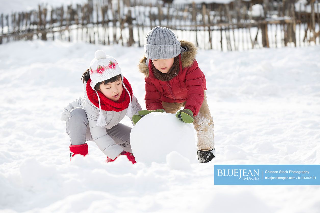 Happy Chinese children rolling snowball together