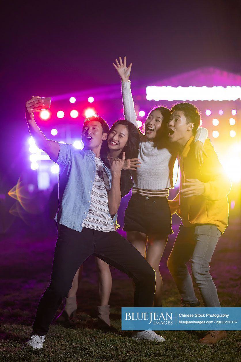 Happy young Chinese friends taking selfie at music festival