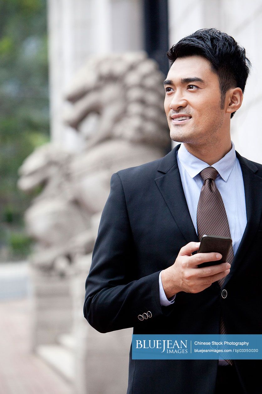 Confident Chinese businessman with smart phone looking at view, Hong Kong