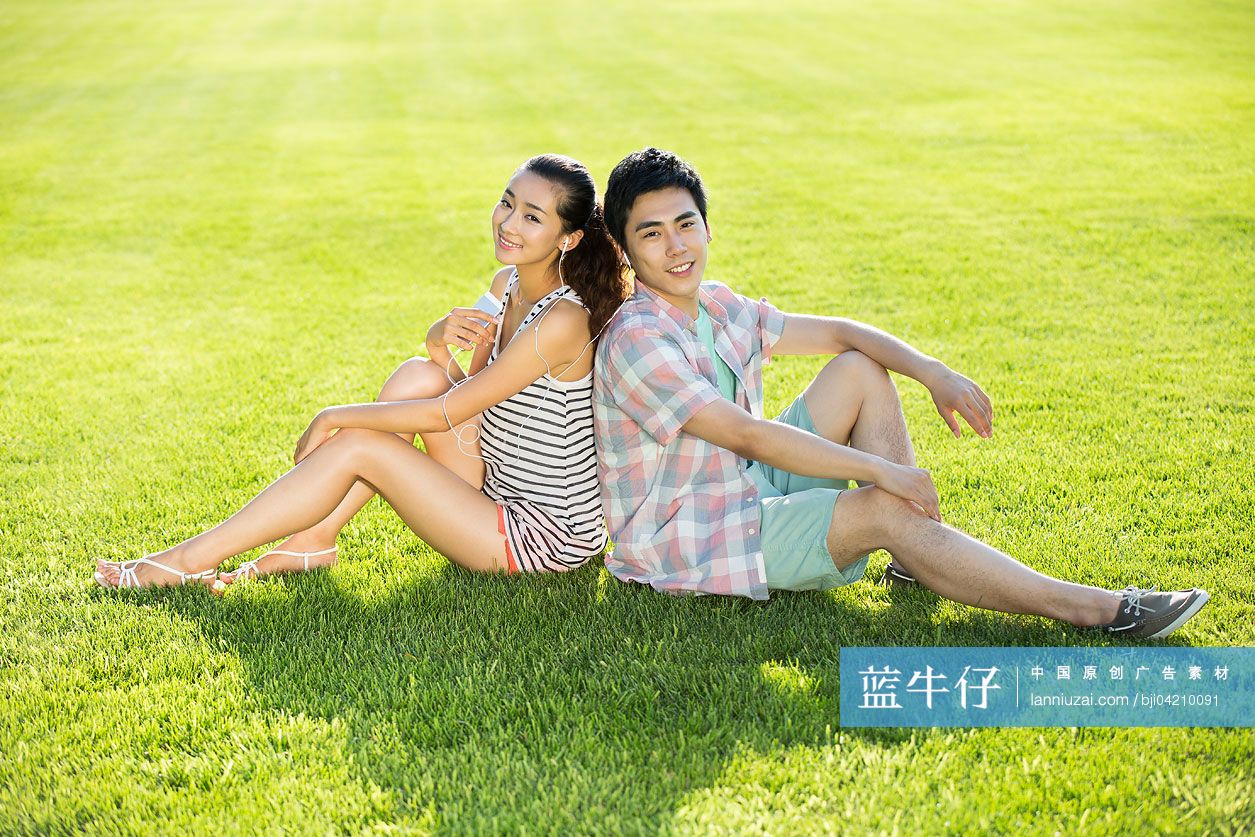 年轻情侣背靠背坐在草地上