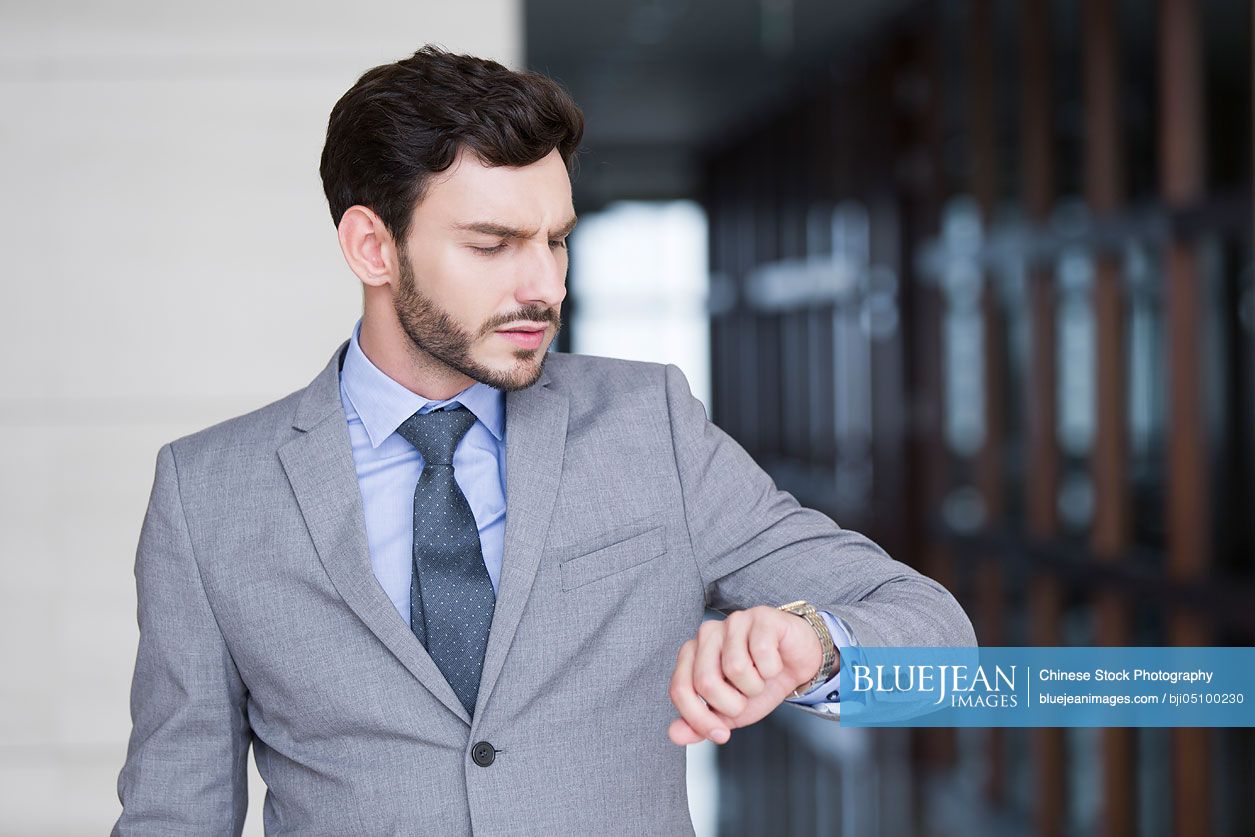Confident Chinese businessman checking the time on wristwatch