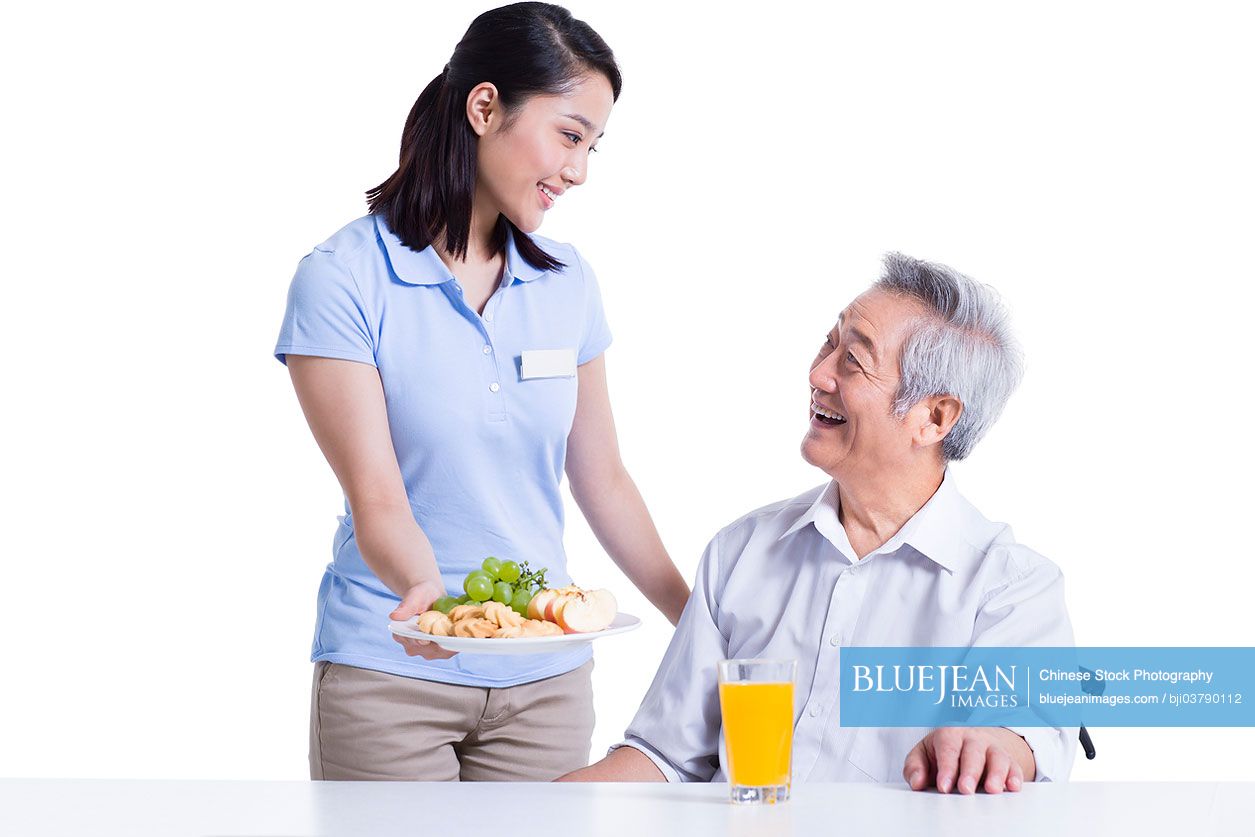 Chinese nursing assistant serving food for disabled senior man