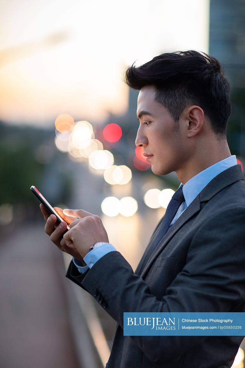 Confident young Chinese businessman using smart phone