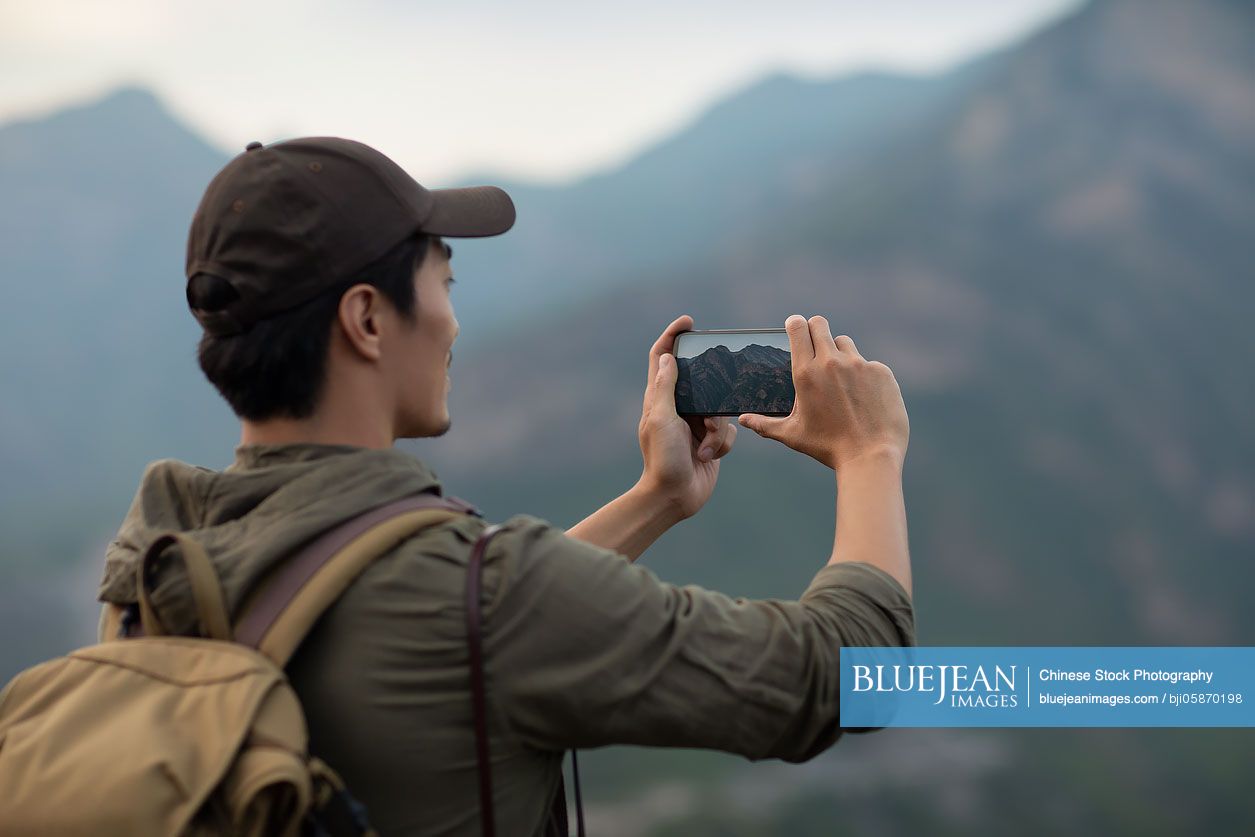 Young Chinese man taking photos with smartphone outdoors