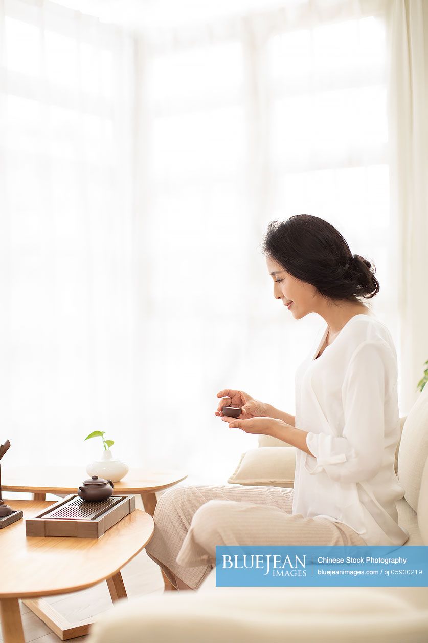 Mature Chinese woman drinking tea in living room
