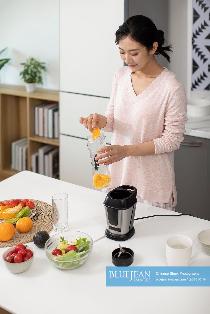Happy young Chinese woman making juice at home