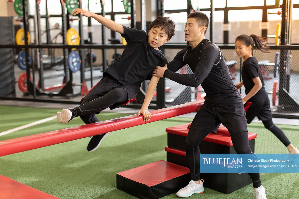 Active Chinese children having exercise class with their coach in gym