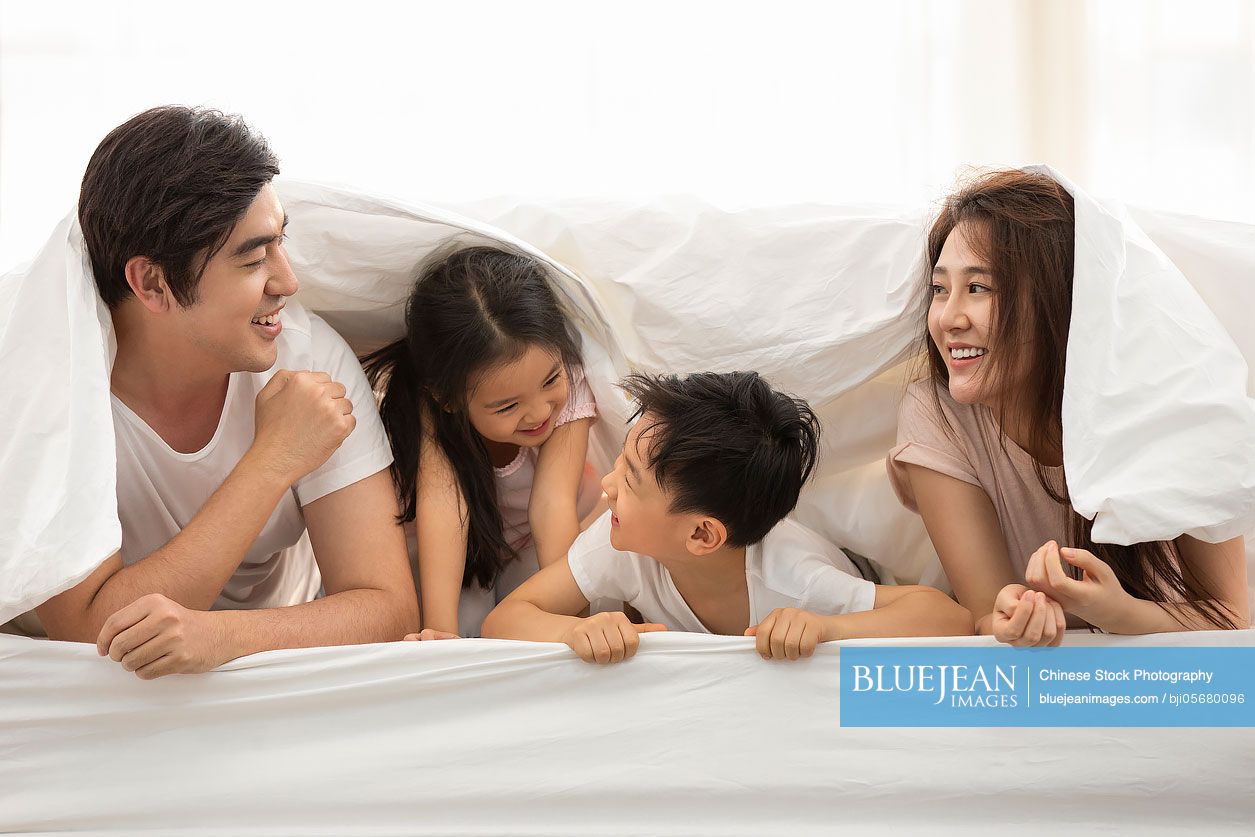 Happy young Chinese family relaxing in bed