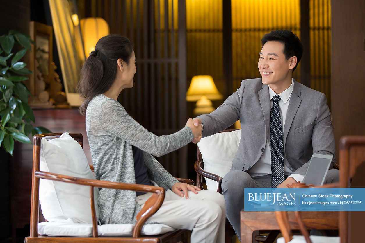 Confident Chinese financial consultant shaking hands with mature woman