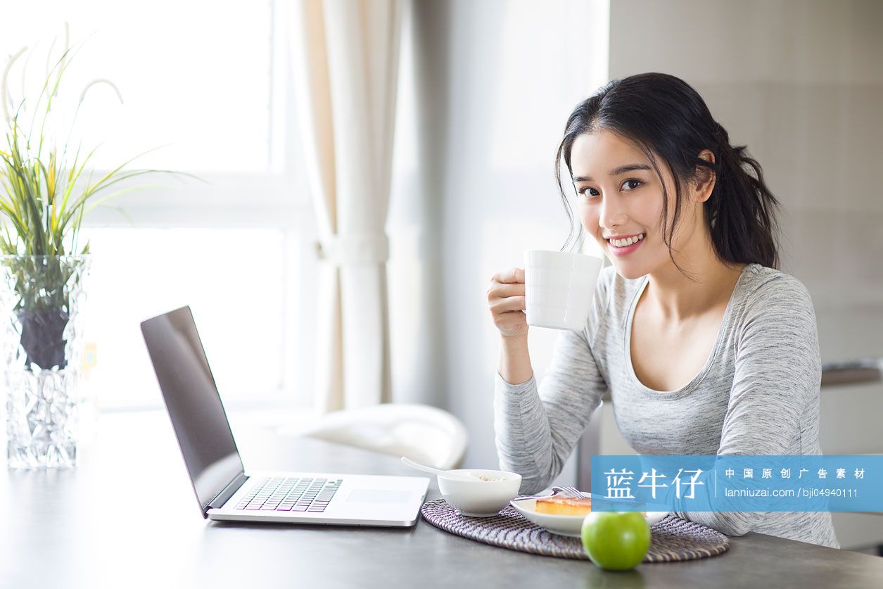 年轻女子一边吃早餐一边使用笔记本电脑