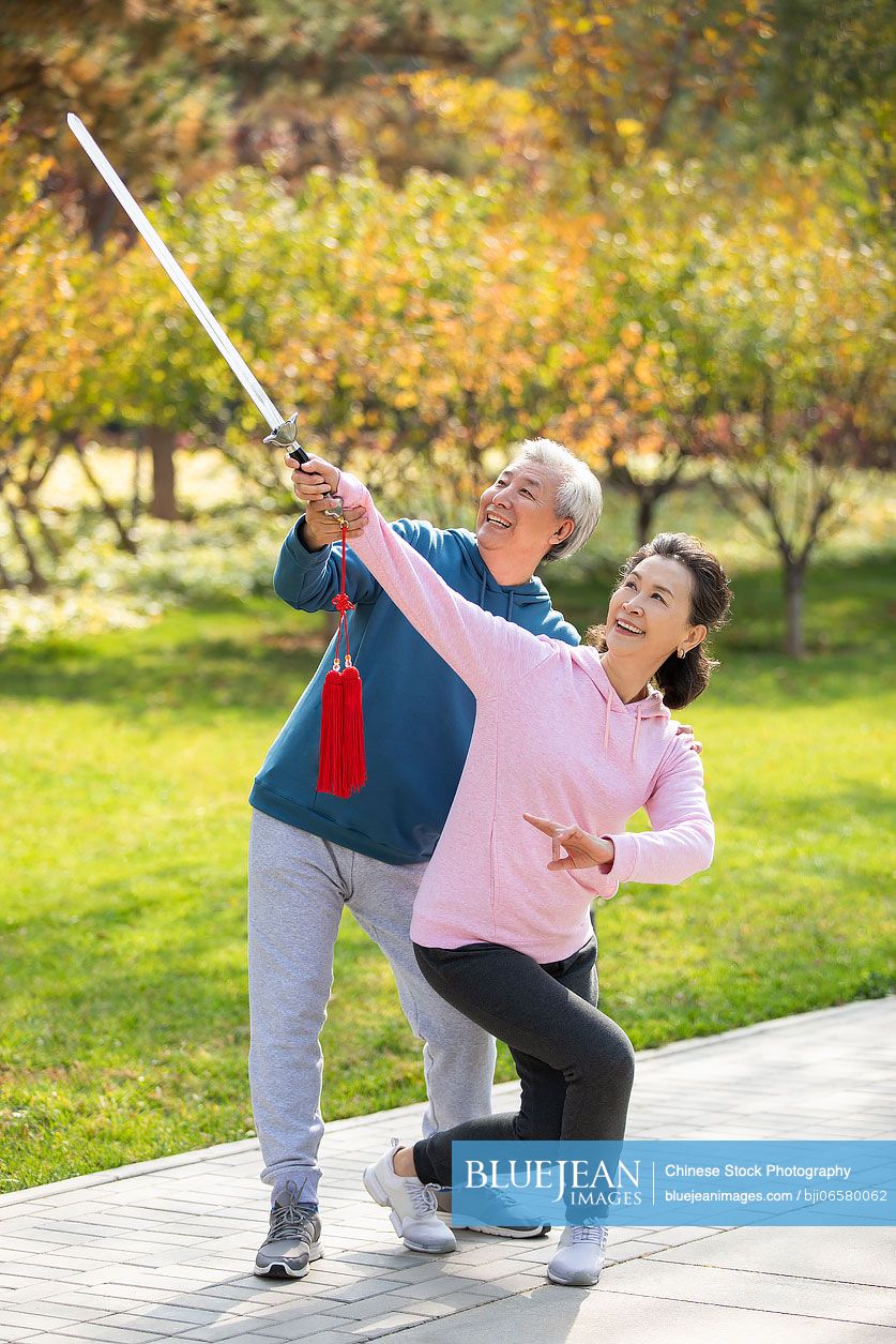 Cheerful senior Chinese adult practicing sword in the park