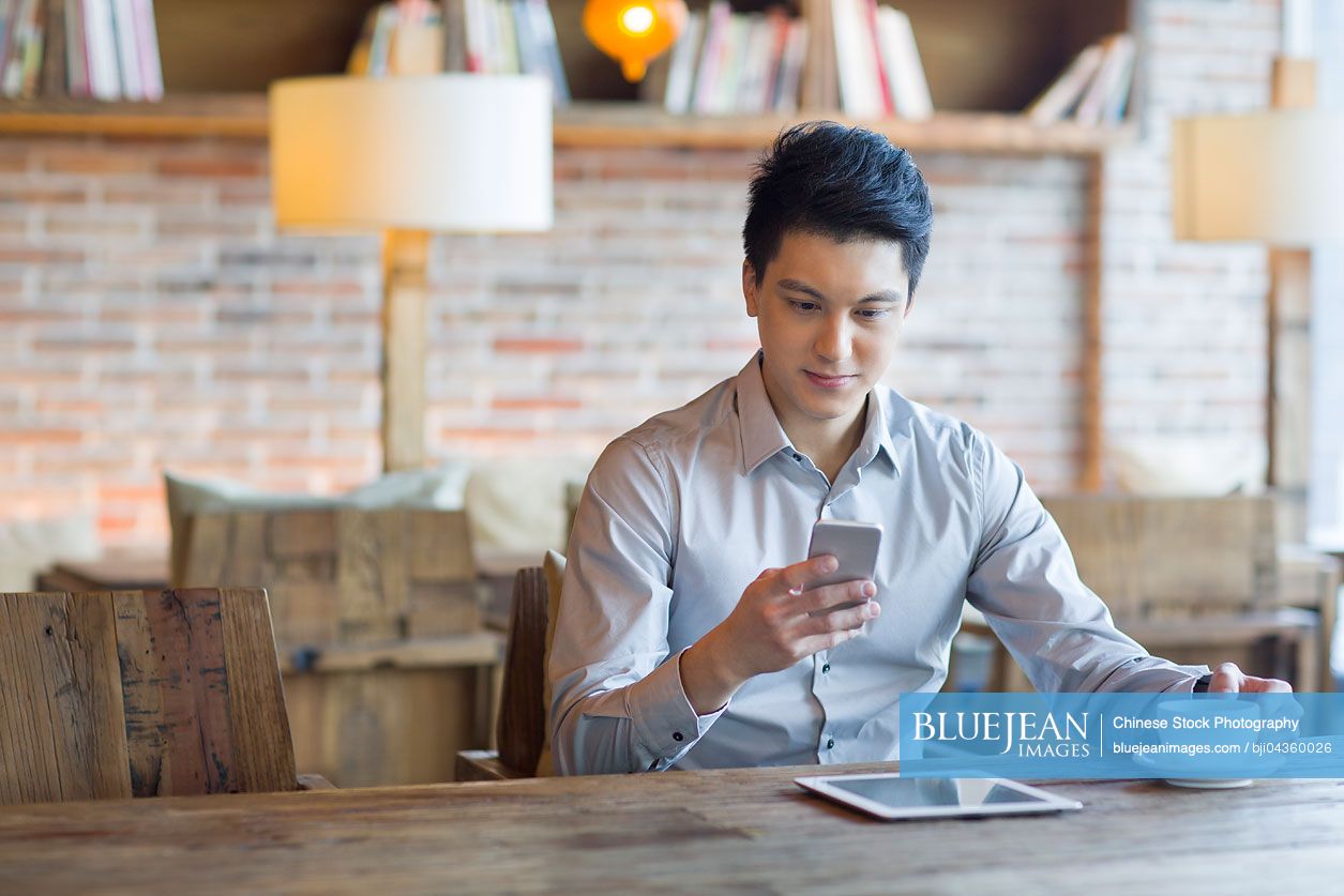 Young Chinese man using smart phone in cafe