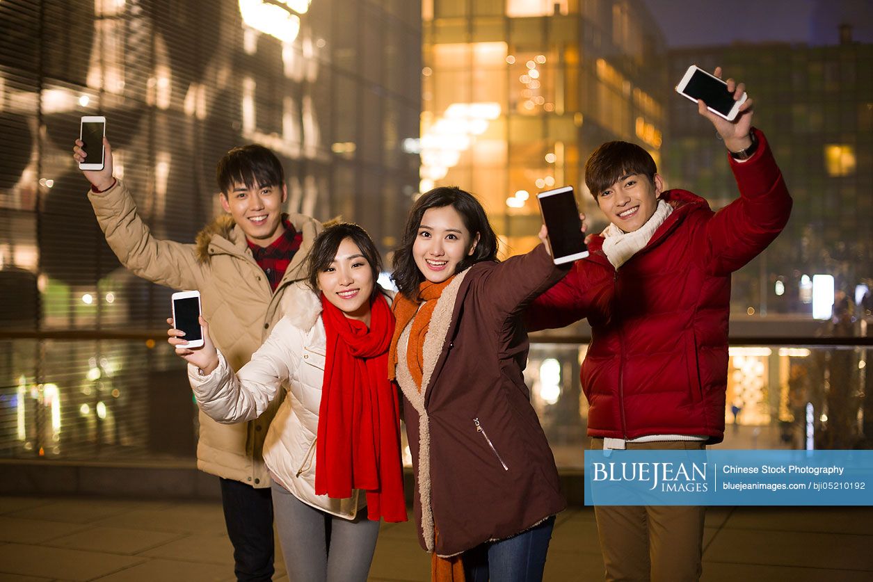 Happy young Chinese friends showing smart phones