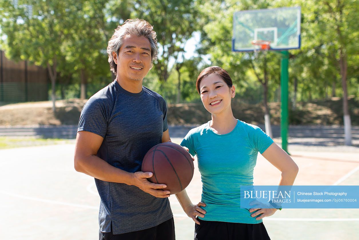 Happy mature Chinese couple playing basketball outdoors