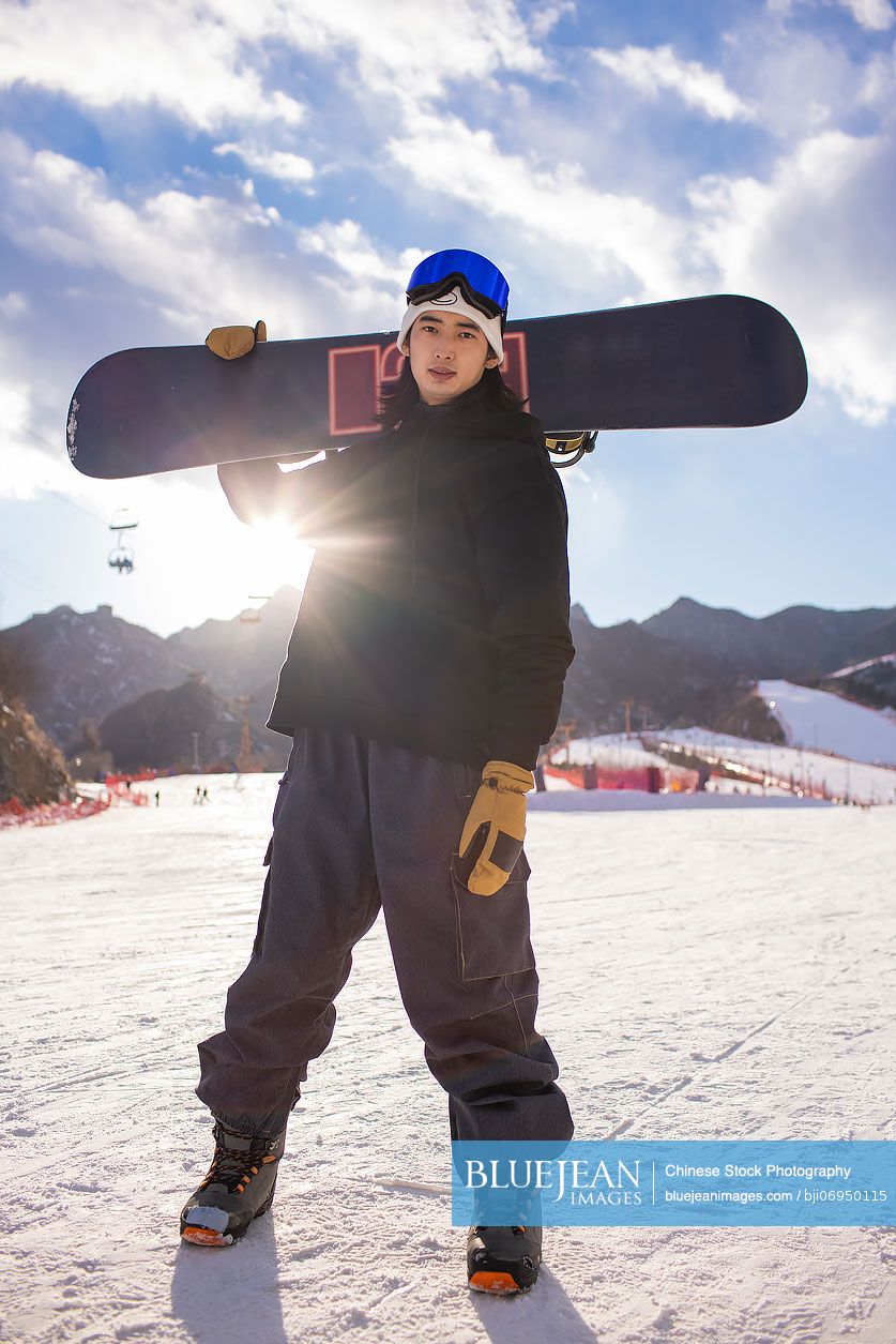 Young Chinese man with snowboard on the snow