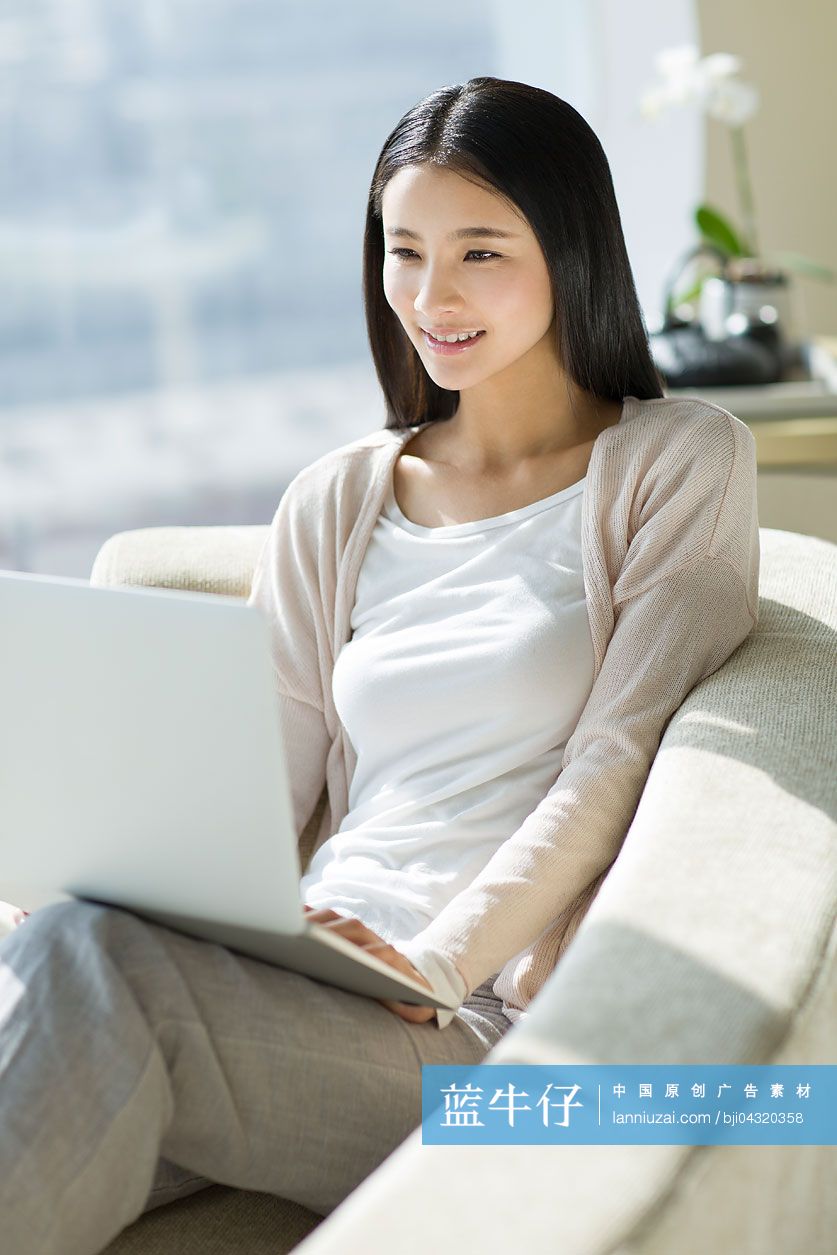 年轻女子坐在沙发上使用笔记本电脑
