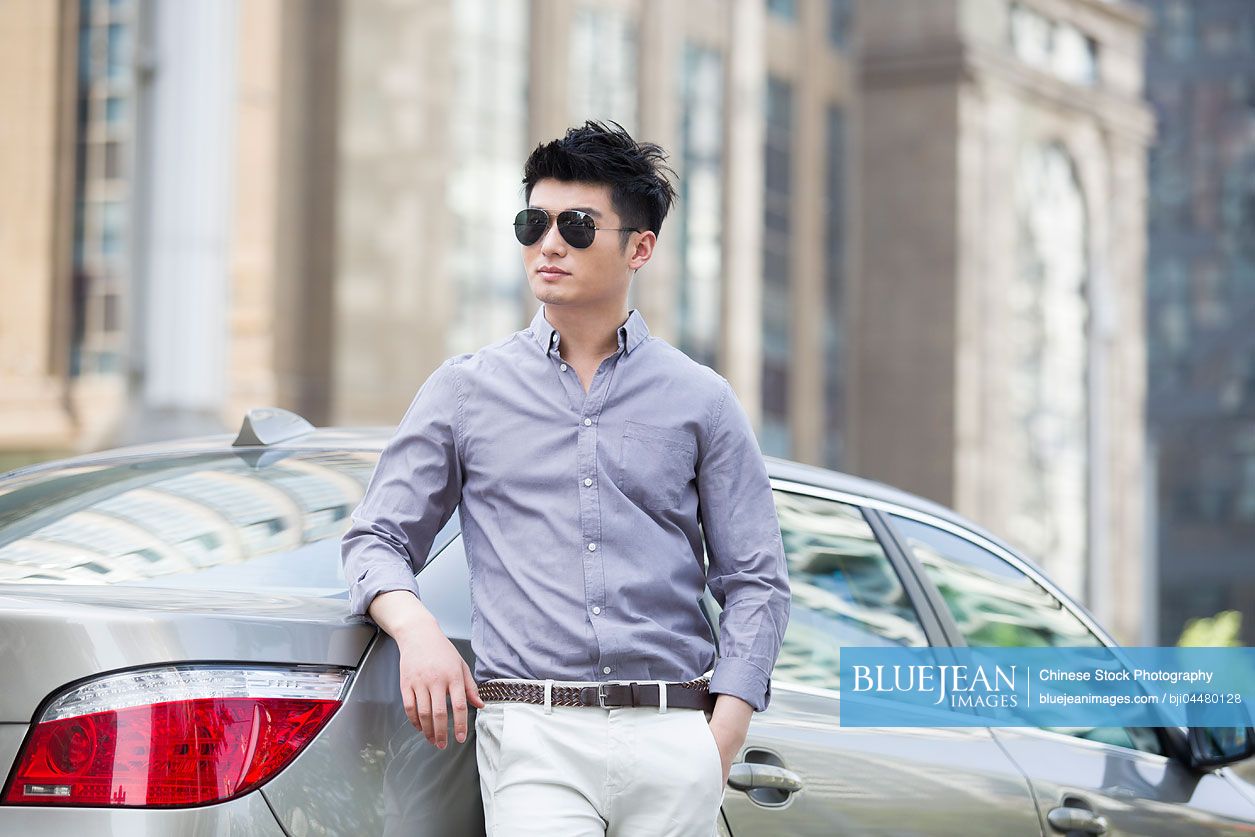 Young Chinese man leaning against his car